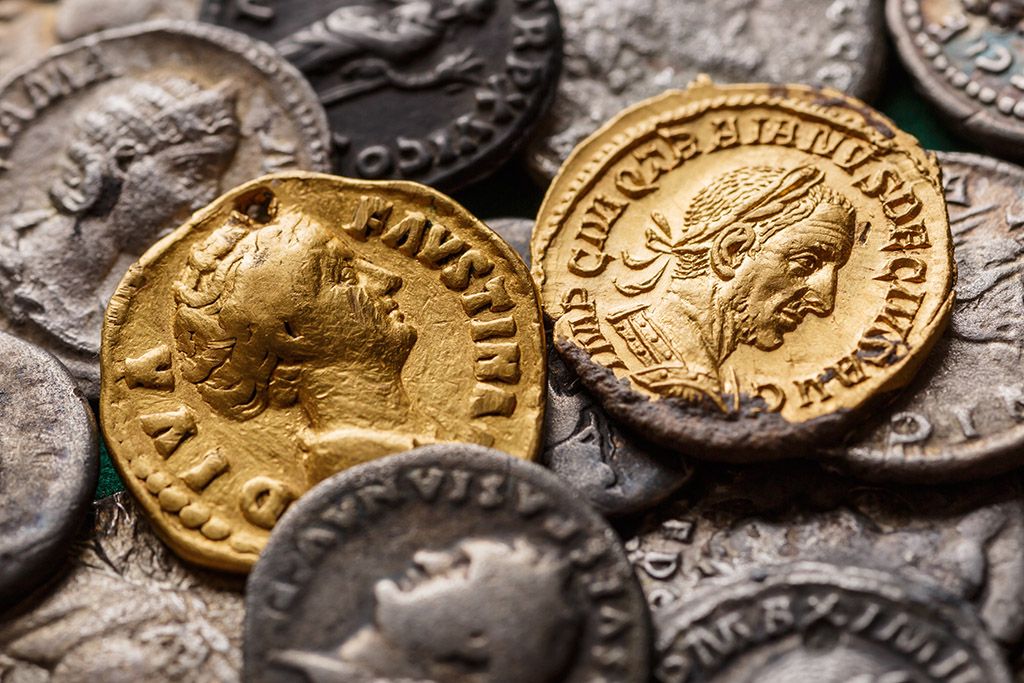 Close up of a hoard of ancient coins, with two gold coins depicting high status individuals of the Roman period